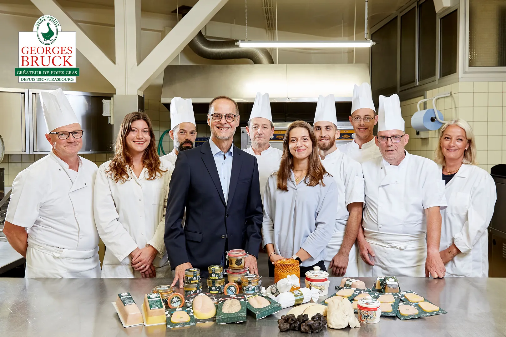 L'équipe de Georges Bruck posant devant des produits de foie gras et des truffes dans une cuisine professionnelle.